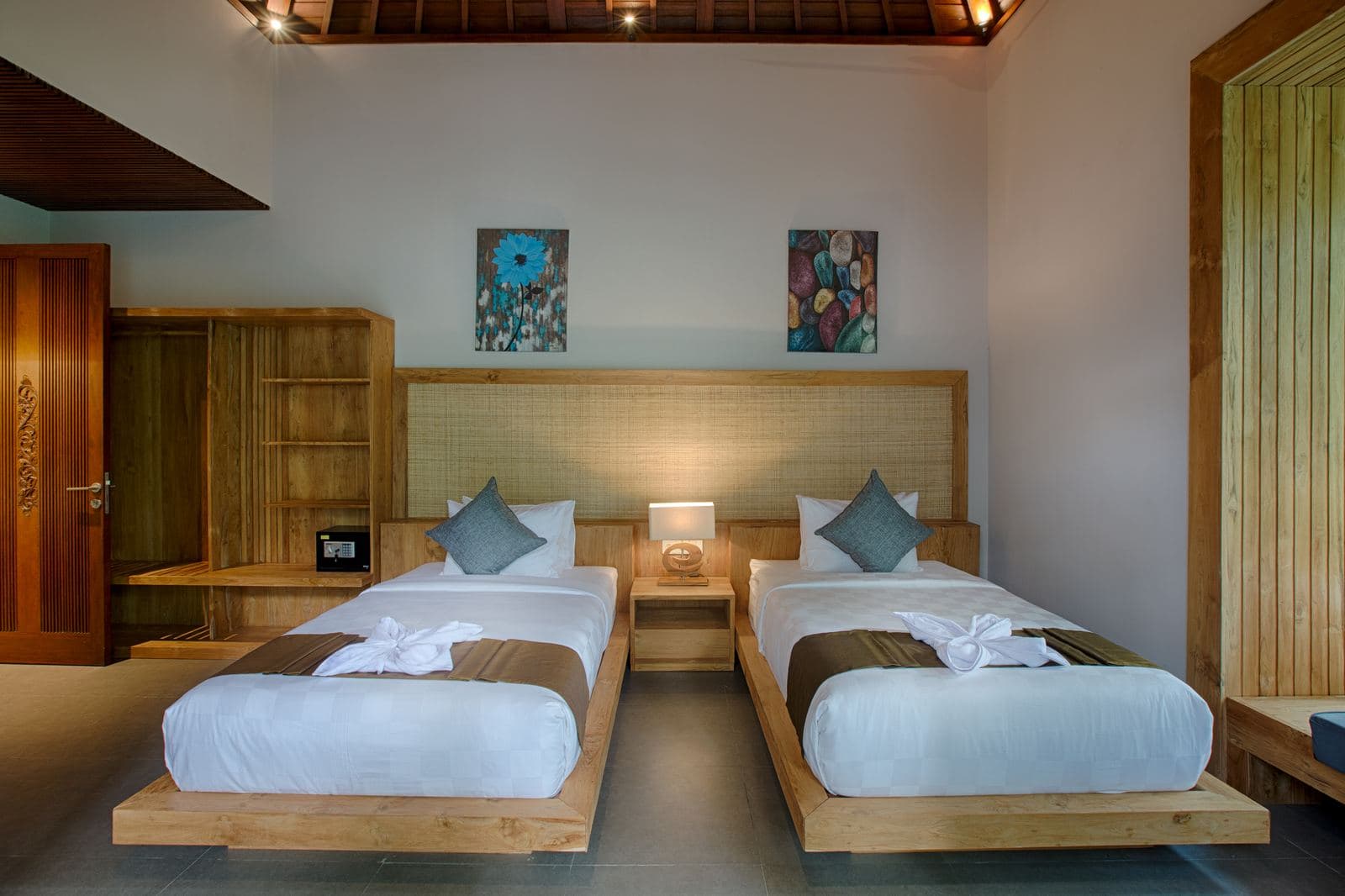 Twin room with two single beds on timber platforms, towels folded at the foot of each and a pair of paintings above