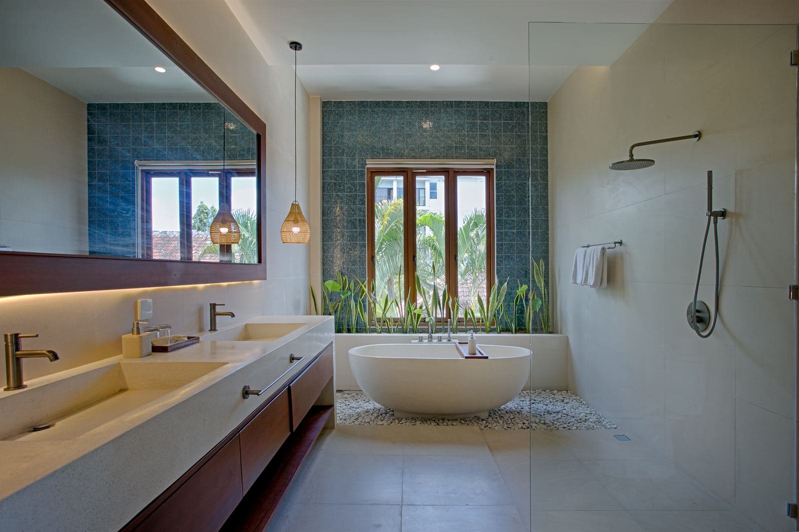 Bathroom with twin basins on a timber vanity, a freestanding oval tub against deep teal tiling and a walk-in shower behind glass