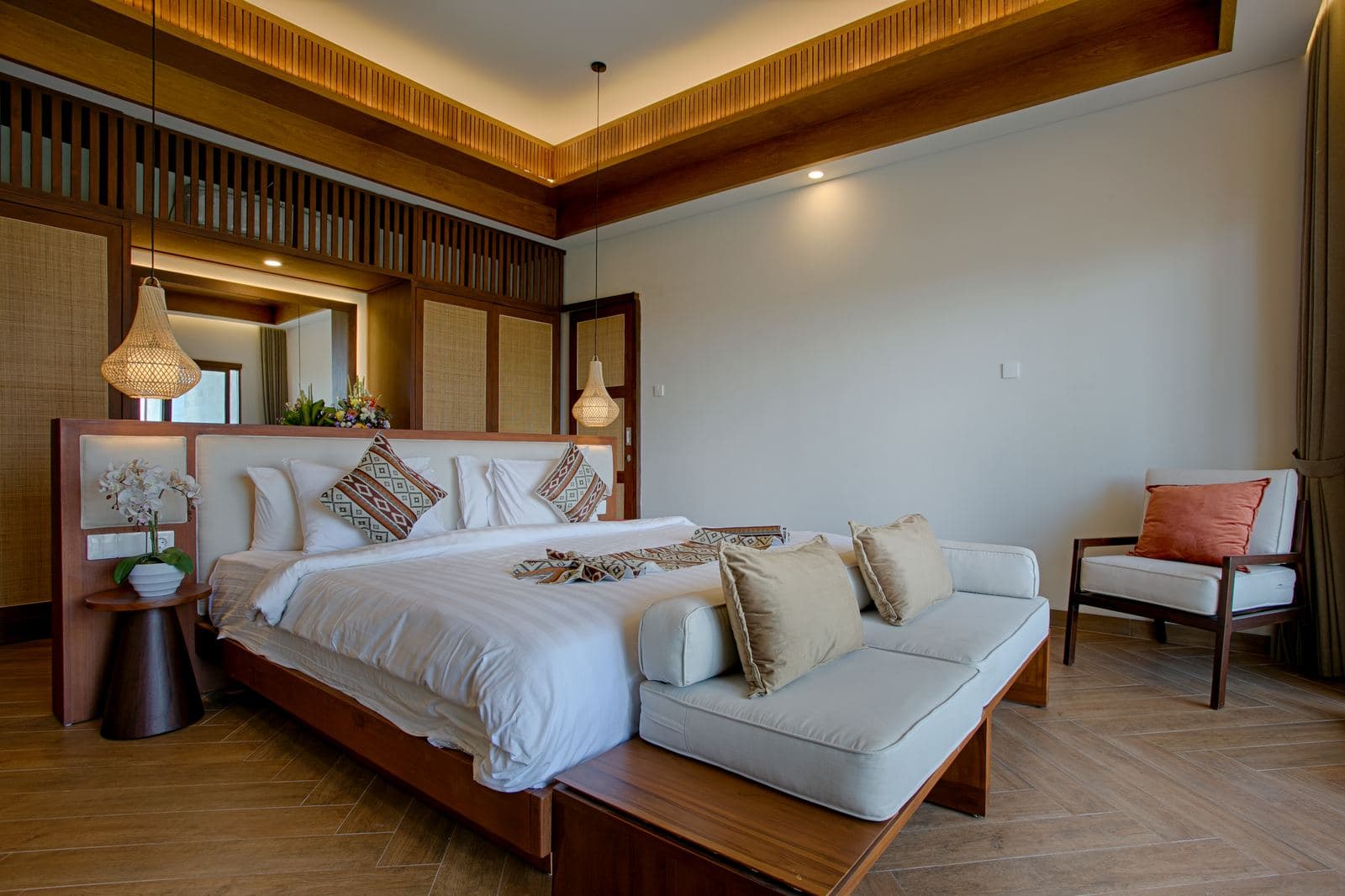 Bedroom with a low platform bed, woven pendant lamps either side, patterned cushions and a long daybed at the foot of the bed