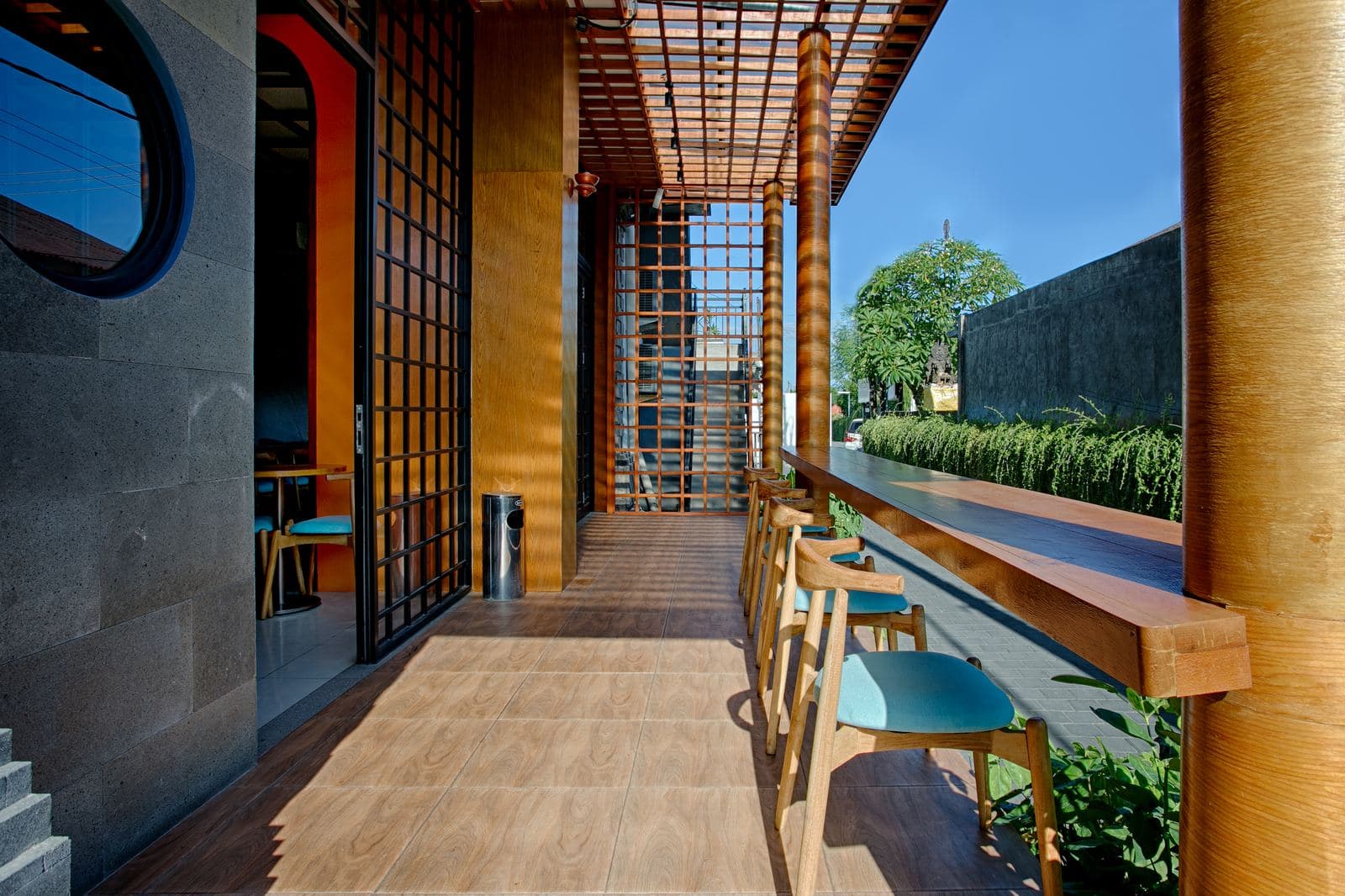 Restaurant walkway under a bamboo pergola, a long counter with stools on one side and a clipped hedge along the other